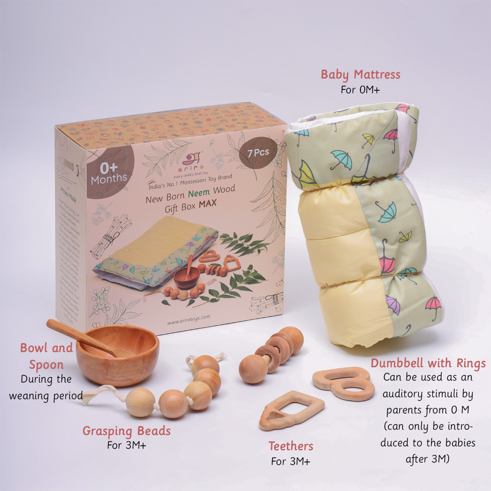 Montessori newborn gift box (0+ months) featuring a soft cotton mattress, neem wood teethers, grasping beads for motor skill development, a dumbbell rattle for sensory stimulation, and a wooden bowl and spoon for early weaning.