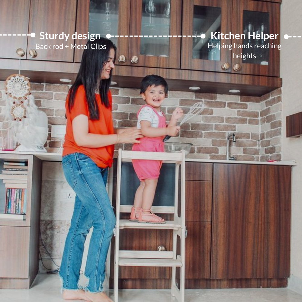 Toddler standing on Ariro Montessori learning tower helping in the kitchen safely while reaching counter height.