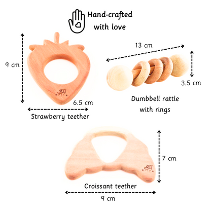 A handcrafted neem wood toy set featuring a strawberry teether, croissant teether, and dumbbell rattle with rings—designed for babies 3 months+ to support safe teething, sensory exploration, and grip development.